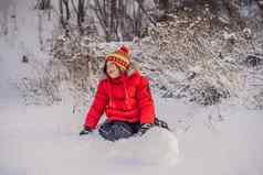 可爱的男孩红色的冬天衣服构建雪人冬天有趣的户外概念