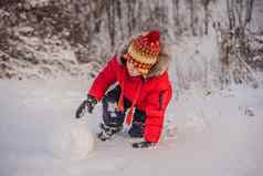 可爱的男孩红色的冬天衣服构建雪人冬天有趣的户外概念