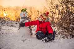 可爱的男孩红色的冬天衣服构建雪人冬天有趣的户外概念