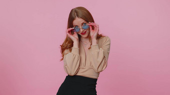 真诚的很酷的快乐的浅黑肤色的女人女孩米色上衣穿太阳镜迷人的微笑粉红色的墙