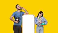 亚洲女孩高加索人的家伙爱会说话的古董手机靠巨大的智能手机空白屏幕孤立的黄色的背景产品放置