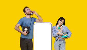 亚洲女孩高加索人的家伙爱会说话的古董手机靠巨大的智能手机空白屏幕孤立的黄色的背景产品放置