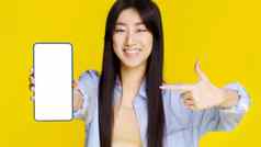 移动电话应用程序广告年轻的亚洲女孩快乐持有智能手机指出白色空屏幕令人兴奋的赢得孤立的黄色的背景产品放置焦点电话