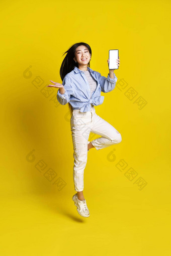 快乐亚洲女孩跳持有智能手机显示白色<strong>屏</strong>幕移动应用程序广告孤立的黄色的背景完<strong>整</strong>的长度肖像快乐的亚洲女孩产品放置