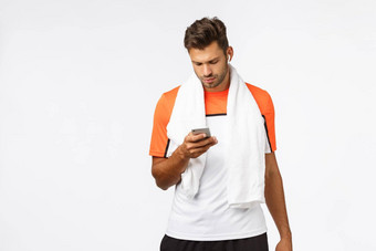 英俊的年轻的运动员体育t恤包装毛巾脖子穿无线耳机搜索健身播放列表有氧运动锻炼智能手机屏幕听音乐锻炼