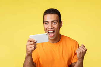 兴奋快乐的家伙赢得拳头泵激动很高兴智能手机屏幕微笑数量实现奖励奖站冠军庆祝黄色的背景