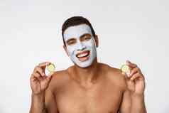 照片快乐的非洲美国男人。面部化妆品面具使有趣的黄瓜孤立的白色背景