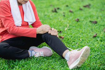 高级亚洲女人膝盖脚踝疼痛运行公园高级亚洲女人坐着地面持有痛苦的膝盖