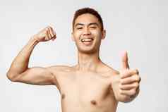 锻炼生活方式健康概念肖像骄傲自负的英俊的亚洲男人。flex肱二头肌强大的健身房显示翘拇指推荐培训程序微笑格子锯