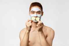 美护肤品水疗中心概念肖像愚蠢的有趣的英俊的亚洲男人。玩黄瓜块应用面部面具放松舒缓的痤疮皮肤化妆品产品
