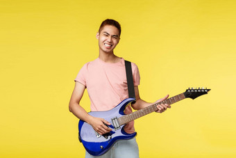 生活方式休闲青年概念让小时无忧无虑的微笑亚洲的家伙玩乐队持有蓝色的电吉他感觉摇滚开始阶段站乐观的黄色的背景