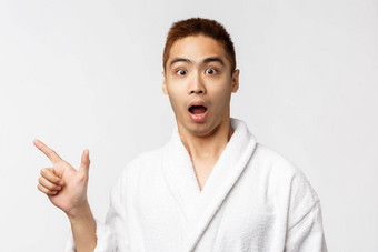 美水疗中心休闲概念肖像惊讶吓了一跳亚洲男人。浴袍开放口感兴趣感兴趣指出手指左显示白色背景