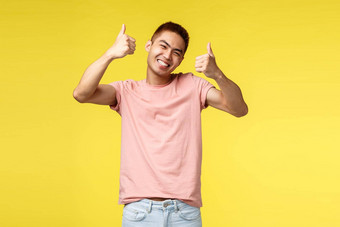 生活方式旅行人概念快乐亚洲男人。粉红色的t恤满意太棒了产品显示竖起大拇指微笑广泛的保证批准促销黄色的背景