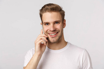 听友好的好看的微笑金发碧眼的高加索人的家伙白色t恤回答调用持有智能手机耳朵会说话的使订单站白色背景