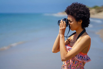 年轻的黑色的女人非洲式发型头发夏天衣服采取图片单反相机海滩