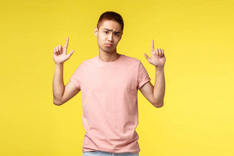 肖像不满意不高兴亚洲的家伙粉红色的t恤指出手指显示失望令人心烦意乱的新闻叹息悲观的相机心烦意乱站黄色的背景