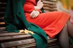 女人橙色衣服绿色外套坐着公园板凳上户外秋天时尚