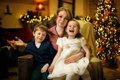 年轻的美丽的金发女郎妈妈孩子们摆姿势扶手椅圣诞节室内