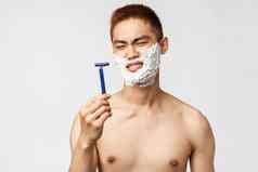 美人卫生概念肖像失望持怀疑态度亚洲男人。扮鬼脸剃须刀不高兴坏剃须叶片应用面部奶油掉胡子