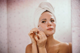 年轻的美丽的女人保湿面部面具采取浴漂亮的有吸引力的女孩毛巾头站前面镜子首页浴室每天卫生皮肤护理