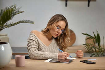 女人眼镜米色毛衣坐着厨房表格杯棕榈平板电脑智能<strong>手机卡</strong>写笔记本特写镜头