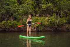 站桨董事会女人桨登机湖站快乐paddleboard蓝色的水行动拍摄年轻的女人桨董事会