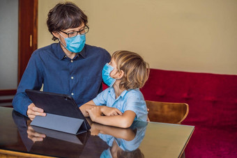 男孩研究在线首页平板电脑父亲帮助学习父亲儿子医疗面具保护coronovirus研究检疫全球流感大流行科维德病毒