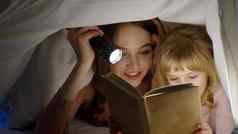 年轻的妈妈。阅读晚安故事童话孩子女儿羽绒被毯子晚上房间