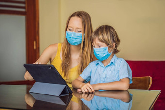 男孩研究在线首页平板电脑妈妈帮助学习妈妈儿子医疗面具保护coronovirus研究检疫全球流感大流行科维德病毒