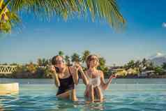 美丽的年轻的女人坐着在游泳池边度假胜地游泳池夏天假期聚会，派对旅游热带国家