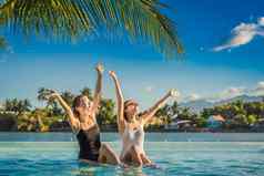 美丽的年轻的女人坐着在游泳池边度假胜地游泳池夏天假期聚会，派对旅游热带国家