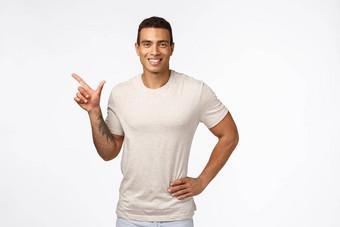 体育健康的人八字胡十一月概念英俊的微笑拉美裔的家伙休闲t恤持有手腰放松指出左咧着嘴笑满意推荐促销做广告产品