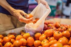 男人。选择西红柿超市塑料袋可重用的袋购买蔬菜浪费概念