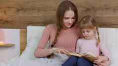年轻的妈妈。阅读晚安故事书童话孩子女儿孩子女孩晚上卧室