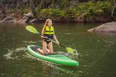 站桨董事会女人桨登机湖站快乐paddleboard蓝色的水行动拍摄年轻的女人桨董事会