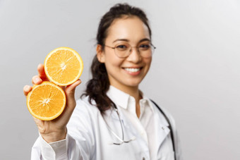 特写镜头肖像亚洲女医生<strong>治疗</strong>师显示块橙色微笑给建议吃健康的食物维生素水果站灰色背景