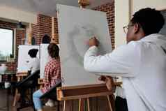 年轻的画家坐着前面白色帆布画花瓶模型