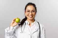 苹果一天医生肖像乐观可爱的亚洲女医生白色外套建议吃健康的食物维生素持有水果微笑相机灰色背景