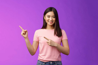 友好的可爱的愉快的亚洲女人显示指示有趣的促销指出左微笑广泛的介绍广告产品站紫色的背景快乐的