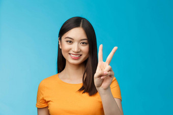 快乐的友好的亚洲女人黄色的t恤微笑广泛的显示数量赢得的地方微笑快乐使外卖订单书坐在站蓝色的背景