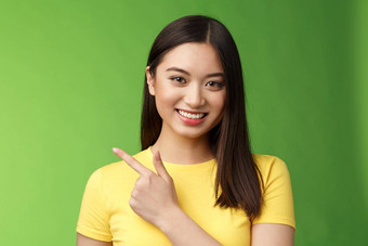 快乐的好看的亚洲浅黑肤色的女人显示优秀的促销机会指出指数手指左微笑很高兴愉快地介绍产品站绿色背景