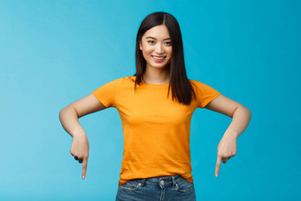 快乐的自信的亚洲女孩黑暗海特卡特穿黄色的夏天t恤介绍促销指出手底广告微笑很高兴分享好链接蓝色的背景