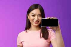 特写镜头快乐的可爱的亚洲女人持有智能手机水平显示电话屏幕介绍太棒了应用程序玩有趣的电话游戏站紫色的背景促进