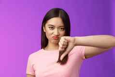 特写镜头不满意不高兴审判的亚洲女孩给拇指扮鬼脸奉承失望推荐可怕的产品抱怨坏服务站紫色的背景