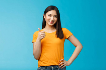 自信快乐的亚洲浅黑肤色的女人女孩显示翘拇指满意给批准喜欢好选择微笑很高兴接受计划积极的判断站蓝色的背景