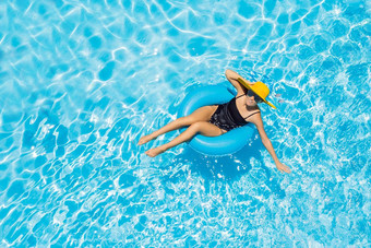 女人坐着游泳池环池浮动大黄色的遮阳帽