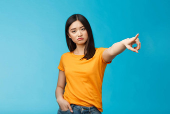 严肃的表情傲慢的不高兴专横的亚洲女孩显示不清楚的指出横盘整理指数手指相机需求离开站蓝色的背景无知的