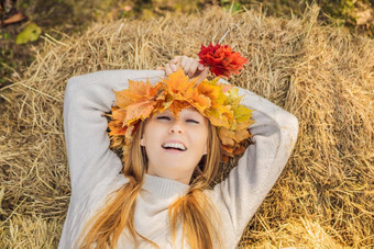 在户外生活方式关闭肖像迷人的金发女郎年轻的女人穿花环秋天叶子干草堆穿时尚的针织套衫花环枫木叶子