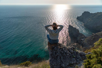 女人旅游享受日落海山景观坐在在户外岩石海穿牛仔裤蓝色的连帽衫健康的生活方式和谐冥想
