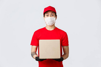 惊讶快递红色的统一的帽t恤持有盒子客户端订单穿医疗面具保护手套安全流感大流行冠状病毒交付男人。带订单